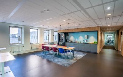 The interior of the kitchen area of a modern office with a long wooden table and chairs